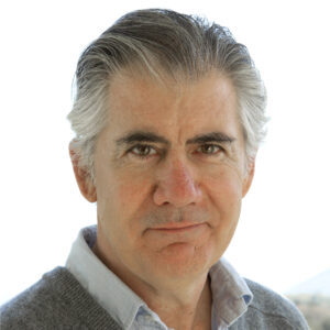 Kevin O’Rourke headshot. White male smiling with thick grey hair, green sweater with blue shirt